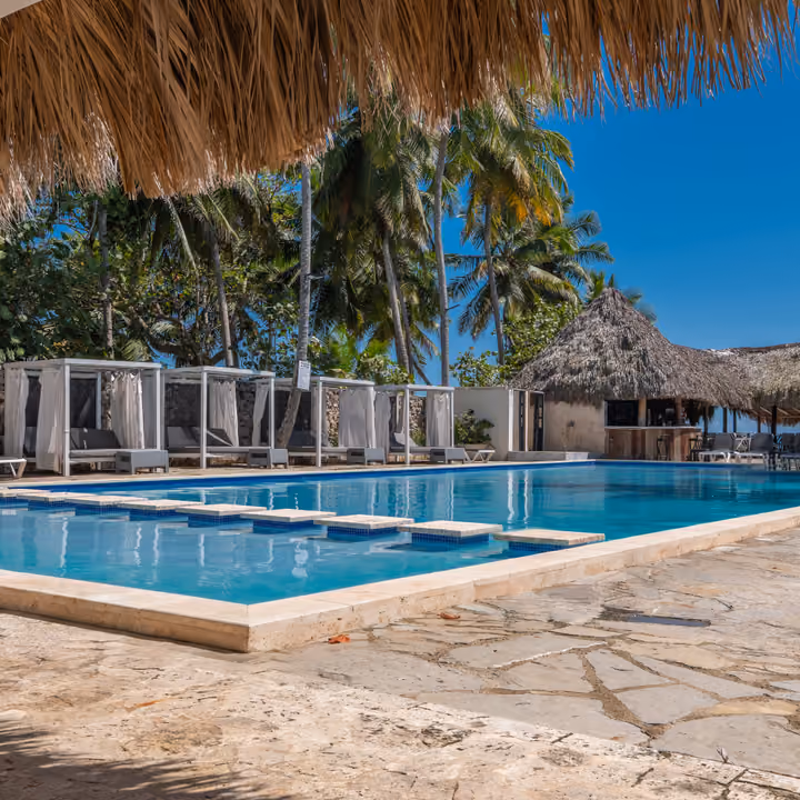 Piscina de Casa Cora con camas balinesas y palmeras