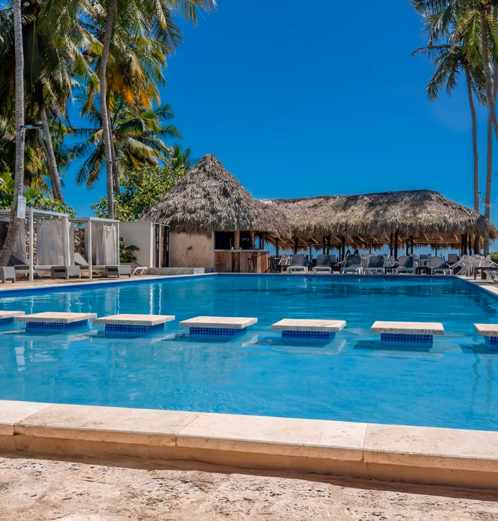 Piscina de Casa Cora con palmeras y cabañas frente al mar